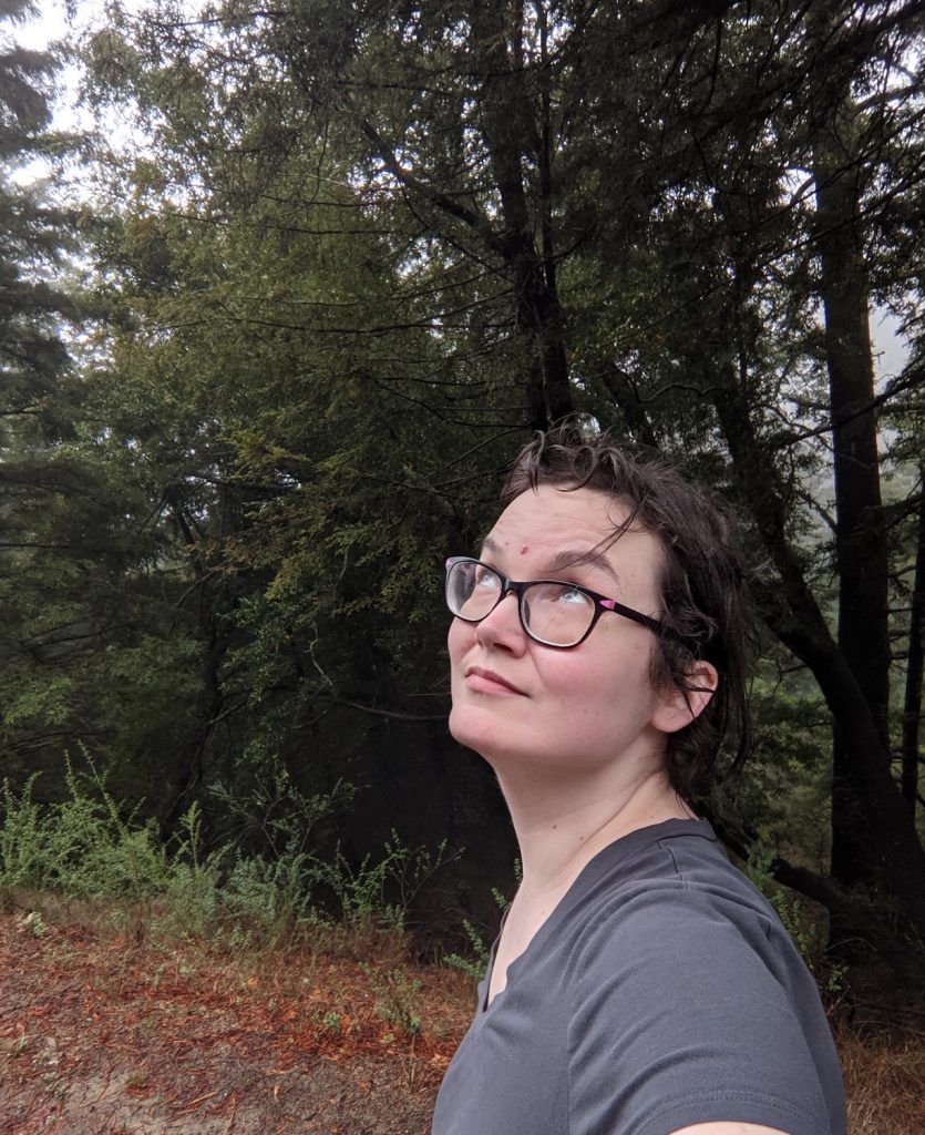 Avory, a non-binary human, looking thoughtfully towards the sky in the woods